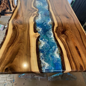 May include: A wooden table top with a blue and white resin river running down the center. The wood is a rich brown color and the resin is clear and glossy.