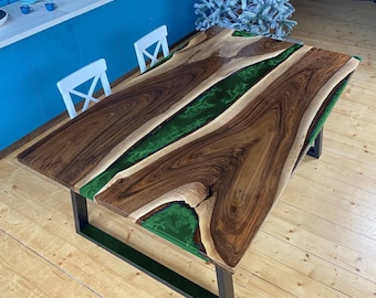 Puede incluir: Una mesa de comedor rectangular con una superficie de madera natural de borde vivo y una incrustación central de resina verde translúcida. La mesa se apoya sobre una base de estructura de metal negro resistente con patas rectangulares.