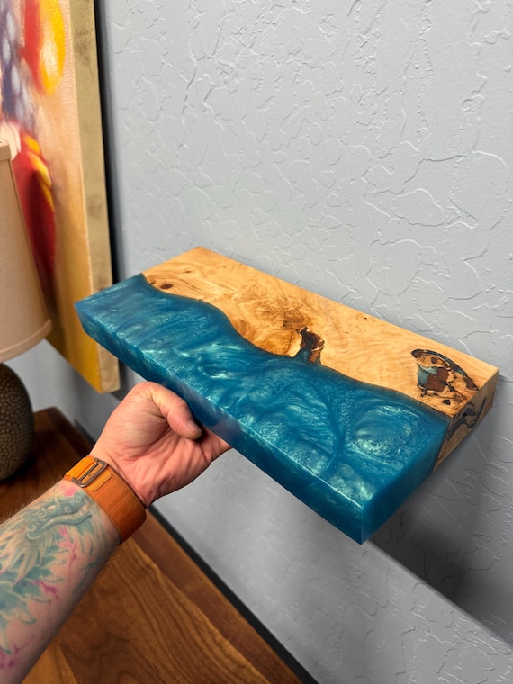 Live-edge walnut or oak floating shelf with an epoxy resin river inlay — functional storage that doubles as wall art, and actually custom-made to order.
