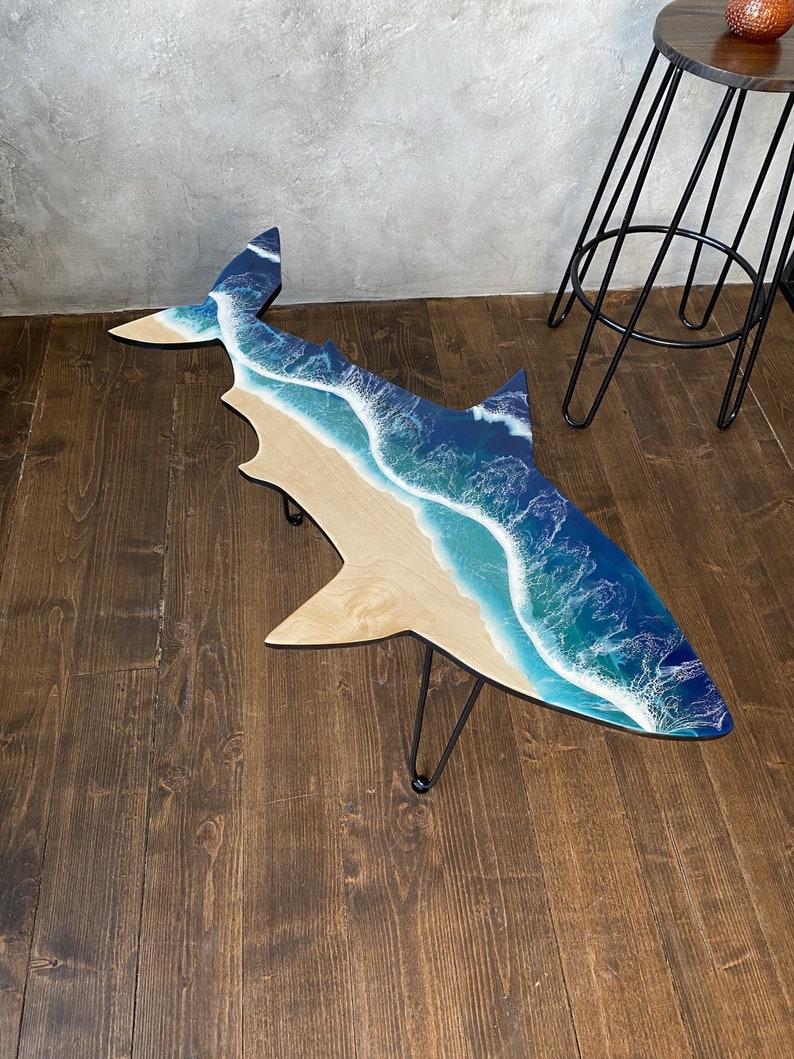 May include: A wooden coffee table shaped like a shark with a blue and white resin ocean wave design.