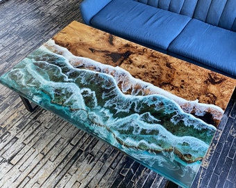 May include: A coffee table with a unique epoxy resin top featuring a blue and white ocean wave design. The table has a dark wood base and is sitting on a wooden floor.