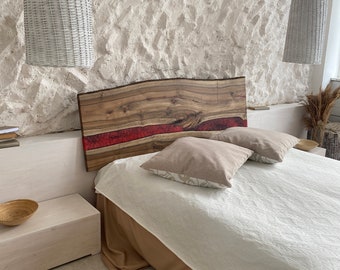 May include: A live edge wooden headboard featuring a horizontal red resin inlay, positioned behind a bed with a white quilted coverlet and two beige square pillows. The headboard displays natural wood grain patterns and a dark brown finish.