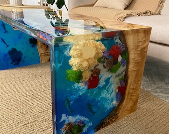 May include: A coffee table with a clear epoxy resin top featuring a blue and green ocean scene with coral, seashells, and fish. The table has a natural wood base.