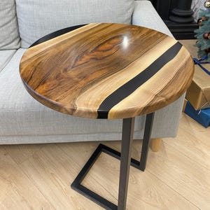 May include: A round side table with a wooden top and black epoxy resin inlay. The tabletop is supported by a black metal frame. The table is approximately 24 inches in diameter.