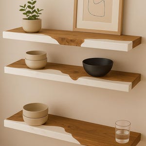 Könnte beinhalten: Drei wandmontierte schwebende Regale aus Naturholz mit einer weißen Harzkante in organischem, wellenförmigem Design. Die Regale tragen eine kleine Topfpflanze, einen gerahmten Kunstdruck, zwei gestapelte beige Schalen, eine schwarze Schale und ein Glas.