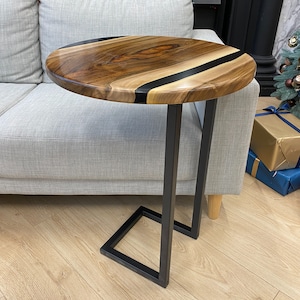 May include: A round side table with a dark wood top featuring a black stripe and a glossy finish. The table has a black metal frame with a C-shaped design, perfect for sliding under a sofa. The table is approximately 20 inches in diameter.