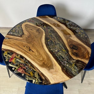 May include: A round wooden table with a live edge design, featuring a clear resin inlay filled with dried flowers. The table is surrounded by three blue velvet chairs. The table's diameter is approximately 48 inches.