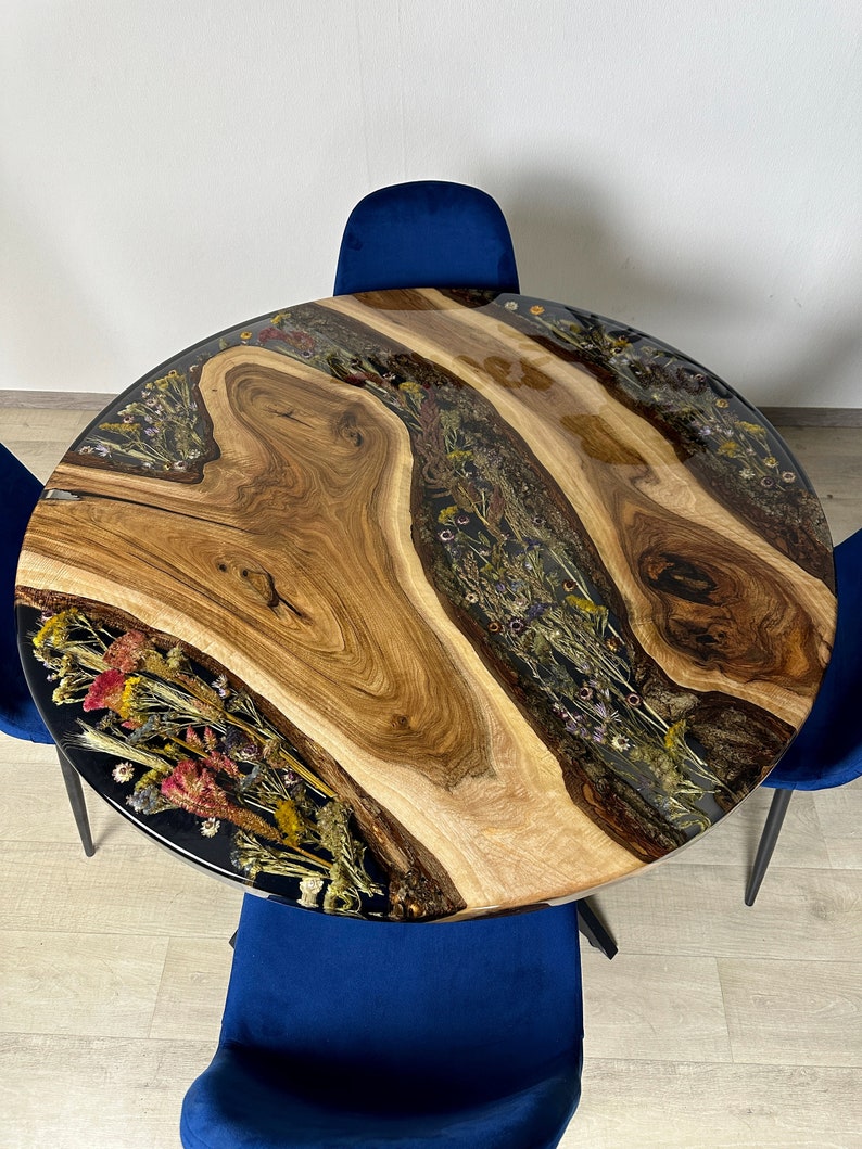 May include: A round wooden table with a live edge design, featuring a clear resin inlay filled with dried flowers. The table is surrounded by three blue velvet chairs. The table's diameter is approximately 48 inches.