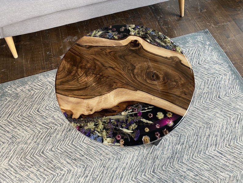 K&ouml;nnte beinhalten: Runder Couchtisch aus Holz mit einer Baumkante und einem schwarzen Harzeinlegearbeiten, gef&uuml;llt mit getrockneten Blumen. Der Tisch hat eine nat&uuml;rliche Holzmaserung und schwarze Metallbeine. Der Tisch hat einen Durchmesser von ca. 91 cm.