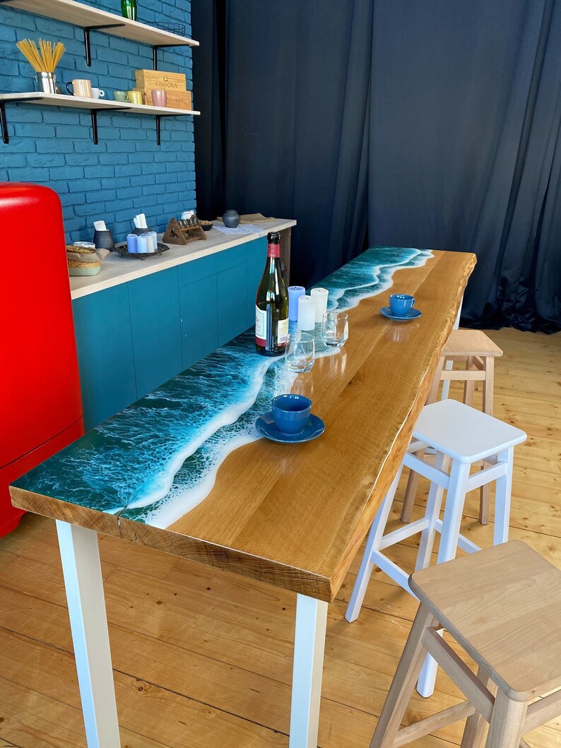 May include: A wooden table with a blue and white epoxy resin ocean wave design. The table has white metal legs and is set up with three wooden stools.