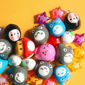 May include: A collection of colourful, hand-painted charms featuring various cartoon characters, including a mushroom, a cat, and a bear. The charms are made of polymer clay and have a glossy finish. They are perfect for adding a touch of whimsy to jewellery, bags, or keychains.