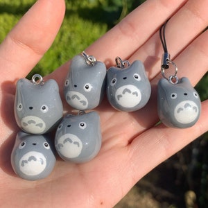 May include: Six grey and white character charms with a white face and black eyes. The charms are attached to silver rings and are hanging from a hand.