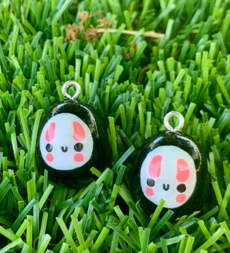 May include: Two black and white charms featuring a cute bunny face design. The bunny has pink ears and cheeks. The charms have a silver loop for hanging.