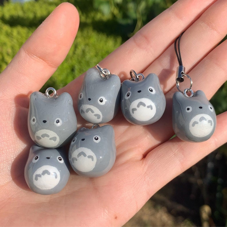 May include: Six grey and white character charms with a white face and black eyes. The charms are attached to silver rings and are hanging from a hand.
