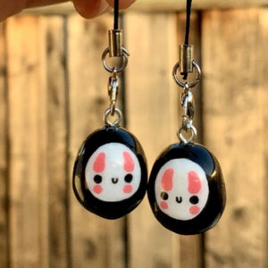 May include: Two black and white charm keychains with a cute bunny face design. The charms are attached to silver chains and black cords.