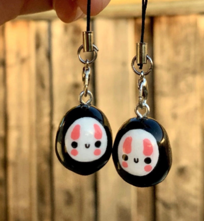 May include: Two black and white charm keychains with a cute bunny face design. The charms are attached to silver chains and black cords.