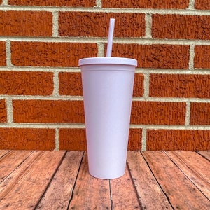 May include: A white, tall, insulated tumbler with a straw. The tumbler has a lid and is sitting on a wooden surface.