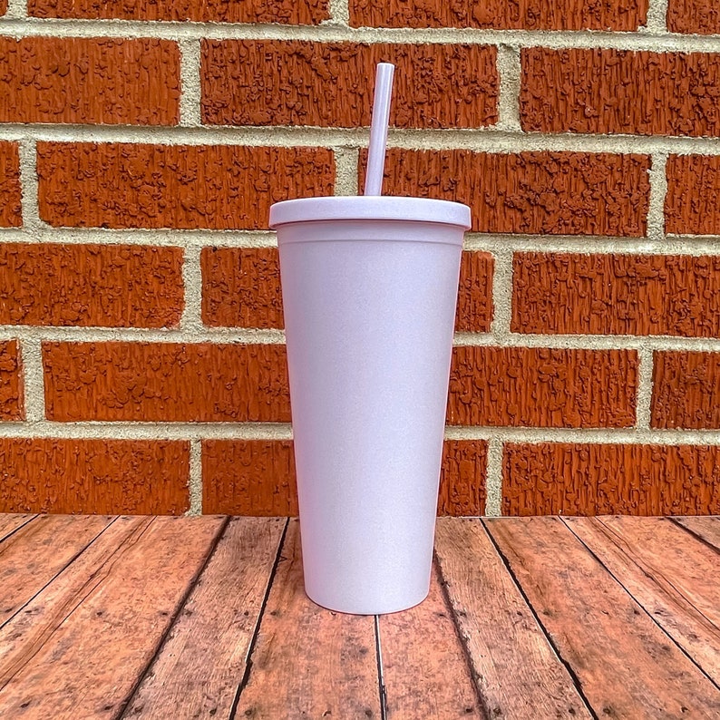 May include: A white, tall, insulated tumbler with a straw. The tumbler has a lid and is sitting on a wooden surface.