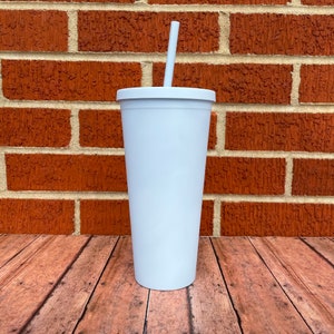 May include: White tumbler with a straw. The tumbler is made of stainless steel and has a smooth, matte finish. It is sitting on a wooden surface.