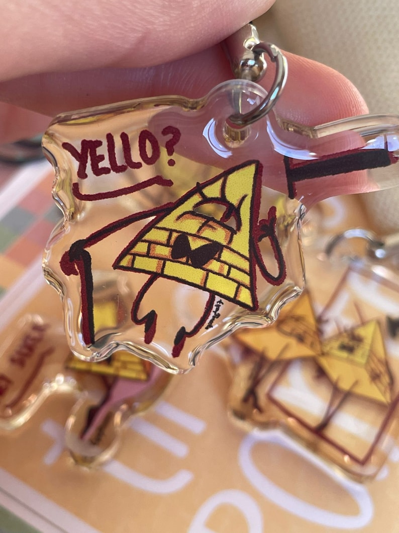 May include: A clear plastic keychain featuring a yellow triangle with a red outline and the text "YELLO?" in red. The triangle has a black eye and a red mouth. The keychain is attached to a silver metal ring.
