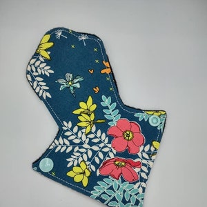 Könnte beinhalten: Ein blauer Stoff-Slipeinlage mit einem Blumendruck mit rosa, gelben und grünen Blumen. Die Einlage hat einen schwarzen Rand und zwei hellblaue Druckknöpfe.