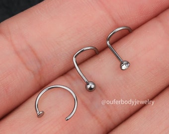 May include: Three nose rings made of stainless steel. One ring is a hoop, and the other two are L-shaped with a ball and a clear gem at the end.