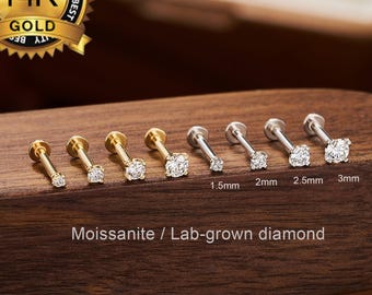 May include: A collection of gold and silver-toned labret studs with clear moissanite stones, ranging from 1.5mm to 3mm in size. The studs are displayed on a dark wooden surface, with a gold seal that reads "14K Gold". The text "Moissanite / Lab-grown diamond" is also visible.