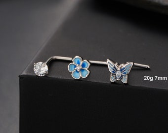 May include: Three nose rings with different designs: a clear round stone, a blue flower, and a blue butterfly. The rings are 7mm long and 20 gauge.