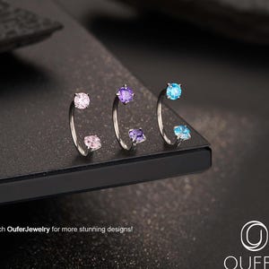 Puede incluir: Tres joyas corporales plateadas con piedras preciosas de colores. Las joyas presentan un diseño curvo con una piedra preciosa en cada extremo. Las piedras preciosas son rosas, moradas y azules. El texto "Search OuferJewelry for more stunning designs!" es visible.