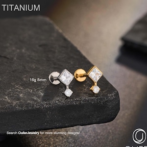 Pode incluir: Dois brincos de titânio com uma pedra preciosa quadrada e transparente e uma pedra preciosa pendurada menor. Um brinco é prateado, o outro dourado. O texto "TITANIUM" está no topo e "16g 8mm" está à esquerda. O texto "Search OuferJewelry for more stunning designs!" está na parte inferior.