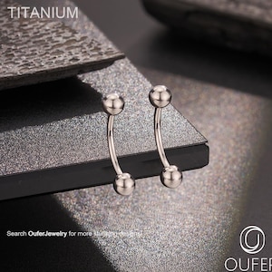 May include: Two curved, silver-coloured eyebrow piercing jewellery with a ball on each end. The word "TITANIUM" is printed at the top. The jewellery is displayed on a textured, dark grey surface. The Oufer Body Jewellery logo is in the bottom right corner.