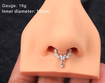 May include: A silver nose ring with a teardrop-shaped pendant and a row of clear cubic zirconia stones. The ring is 16 gauge and has an inner diameter of 10mm.  Gauge: 16g Inner diameter: 10mm