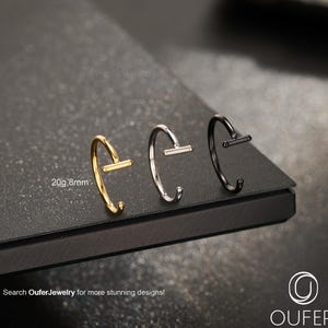 Peut inclure: Trois anneaux de nez en or, argent et noir. Chaque anneau a une barre droite sur le dessus. L'anneau doré est marqué "20g, 8mm". L'image contient également le texte "Search Oufer Jewelry for more stunning designs!"