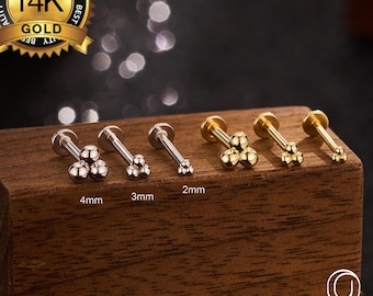 May include: A collection of gold and silver-toned body jewelry studs. Each stud features a cluster of small spheres. Sizes are labeled as 2mm, 3mm, and 4mm. A gold seal reads "14K GOLD" and "BEST QUALITY". The brand name "OUFER BODY JEWELRY" is also visible.