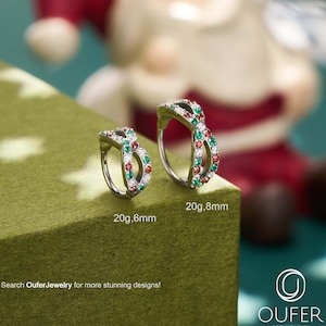 以下が含まれることがあります： 赤、緑、白の宝石が付いた2つのシルバーカラーのボディジュエリーリング。1つは20g、6mm、もう1つは20g、8mmと表示されています。「Search OuferJewelry for more stunning designs!」というテキストが表示されています。