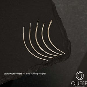 May include: A collection of silver-colored body jewelry, curved and slender, arranged on a dark, textured surface. The jewelry is displayed in a fan-like arrangement. The text "Search OuferJewelry for more stunning designs!" is visible.