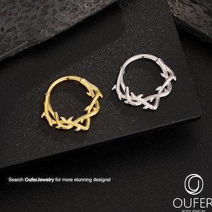 May include: Two body jewellery rings, one gold-toned and one silver-toned, each with a decorative vine-like design. The rings are displayed on a dark surface. The text "Search OuferJewelry for more stunning designs!" is visible.