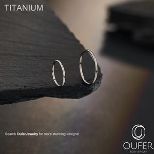 Op de afbeelding: Twee zilveren titanium oorringen op een donkere, getextureerde ondergrond. Het woord "TITANIUM" staat bovenaan. De tekst "Search OuferJewelry for more stunning designs!" staat onderaan, met het Oufer Body Jewelry logo.