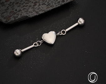 May include: A silver industrial barbell body piercing with a heart-shaped charm in the center. The barbell has two round ball ends and is connected to the heart charm with small chain links. The jewelry is displayed on a black surface.