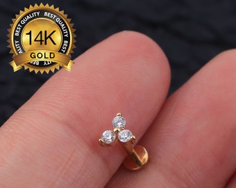 May include: Gold 14K  triple prong stud earring with three clear cubic zirconia stones.  The earring is shown on a finger.