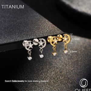 Puede incluir: Pendientes de titanio con diseño de estrella y media luna, cada uno con una circonita colgante. Disponibles en plata y oro. El texto "Titanium" es visible. Los pendientes miden 5,5 mm x 2,5 mm. Busca OuferJewelry.