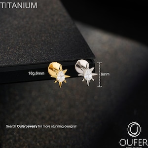 Può includere: Due orecchini a lobo in titanio. Uno è color oro, l'altro color argento. Ogni orecchino presenta un design a stella con una gemma trasparente centrale e misura 6 mm. Il testo "TITANIUM" e "18g,6mm" sono visibili.