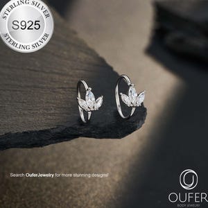 May include: Two sterling silver hoop earrings, each with a floral arrangement of clear, marquise-cut gemstones. The earrings are presented on a dark, textured surface. The image includes the text "STERLING SILVER S925 STERLING SILVER".