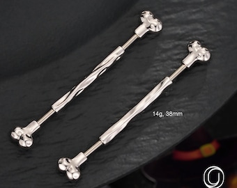 May include: Two silver-colored body jewelry pieces, each with a bone-shaped end and a twisted shaft. The jewelry is 14g and 38mm long. The pieces are displayed on a dark surface, with the brand name "OUFER BODY JEWELRY" visible.