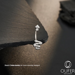 May include: A silver-toned curved barbell belly ring featuring a snake-shaped charm encrusted with small clear stones. The top ball of the jewelry is also adorned with clear stones. The text "Search OuferJewelry for more stunning designs!" is visible.