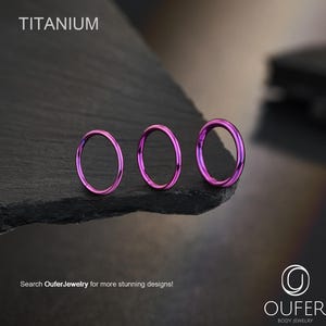 May include: Three purple titanium hoop earrings displayed on a dark, textured surface. The word "TITANIUM" is at the top. The text "Search OuferJewelry for more stunning designs!" is at the bottom, along with the Oufer Body Jewelry logo.
