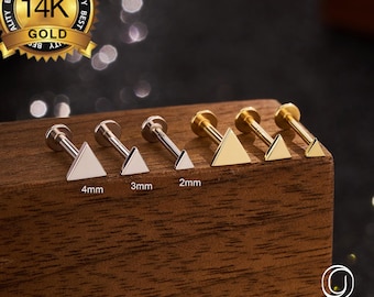 Puede incluir: Una colección de pendientes triangulares para el cuerpo en tonos plateados y dorados. Los tamaños varían de 2 mm a 4 mm. La imagen incluye un sello dorado que dice "14K GOLD" y la marca "OUFER BODY JEWELRY".