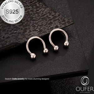 Puede incluir: Dos piezas de joyería corporal plateadas en forma de herradura con una pequeña bola en cada extremo. La joyería está hecha de plata de ley S925. La imagen incluye el texto "Search OuferJewelry for more stunning designs!"