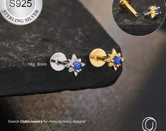 May include: Two star-shaped body jewelry studs. One is silver with a blue gem, the other is gold with a blue gem. The image includes a close-up of the jewelry and a logo that says "OUFER BODY JEWELRY". The text says "STERLING SILVER S925".
