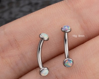 Puede incluir: Dos piezas de joyería corporal de barra curva plateada con piedras preciosas que parecen opales. La joyería es de calibre 16 y 8 mm de largo. El texto "@outerbodyjewelry" es visible en la imagen.